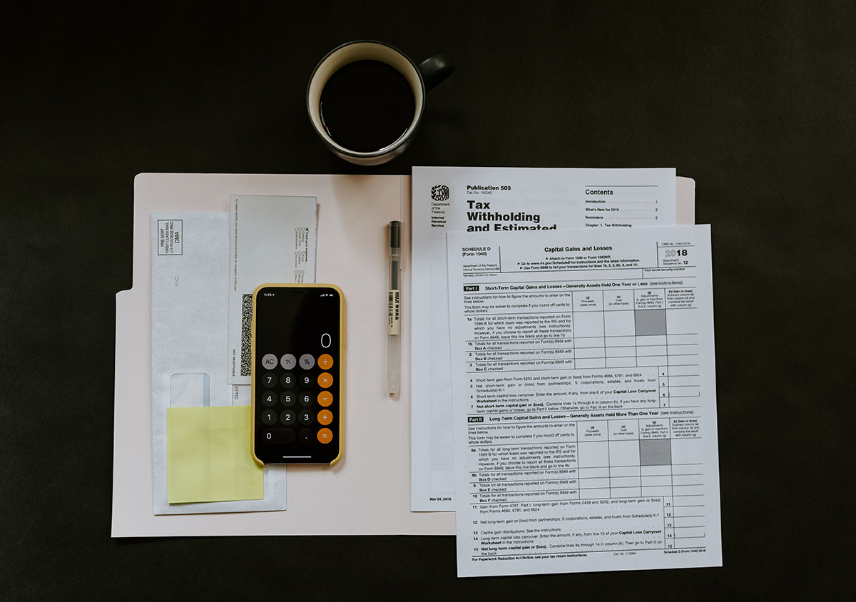 coffee mug, iphone with calculator app open and folder with tax documents on table